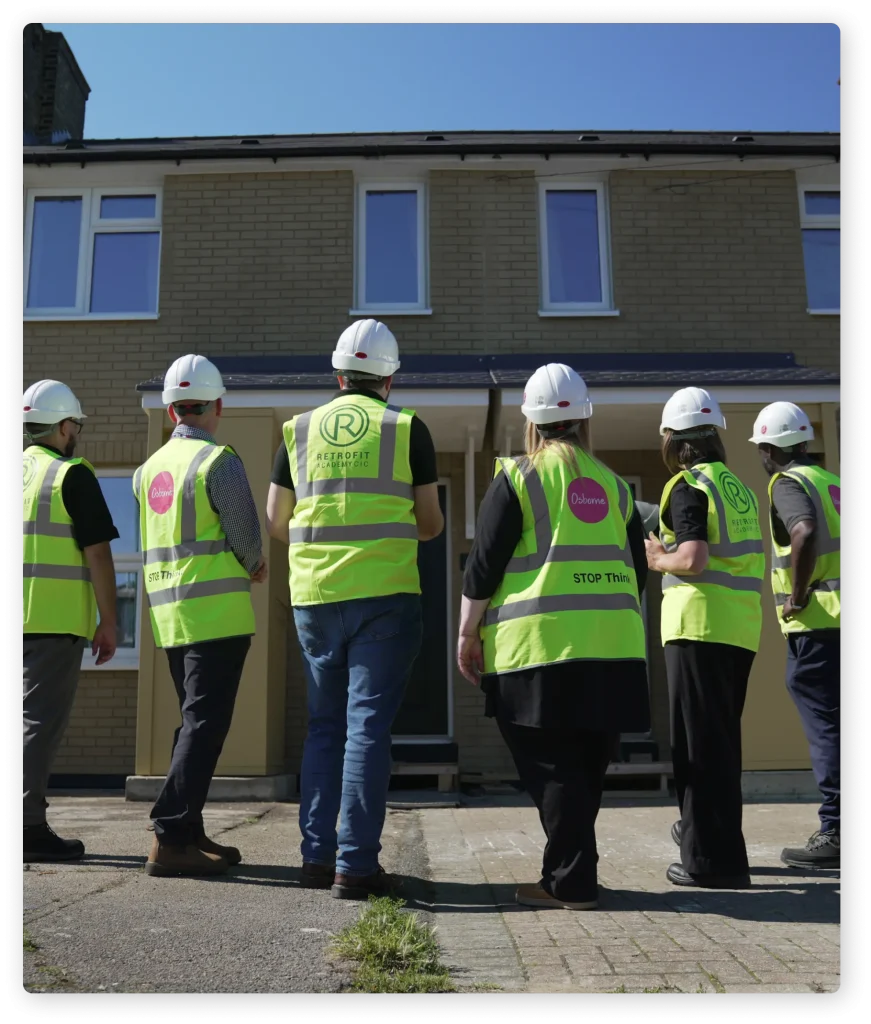 Construction workers all wearing hard hats and hi-vis staring at a house.