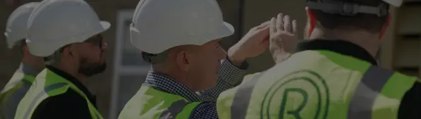Four individuals are standing in a row wearing hard hats, hi-vis vests and are facing away from the camera.